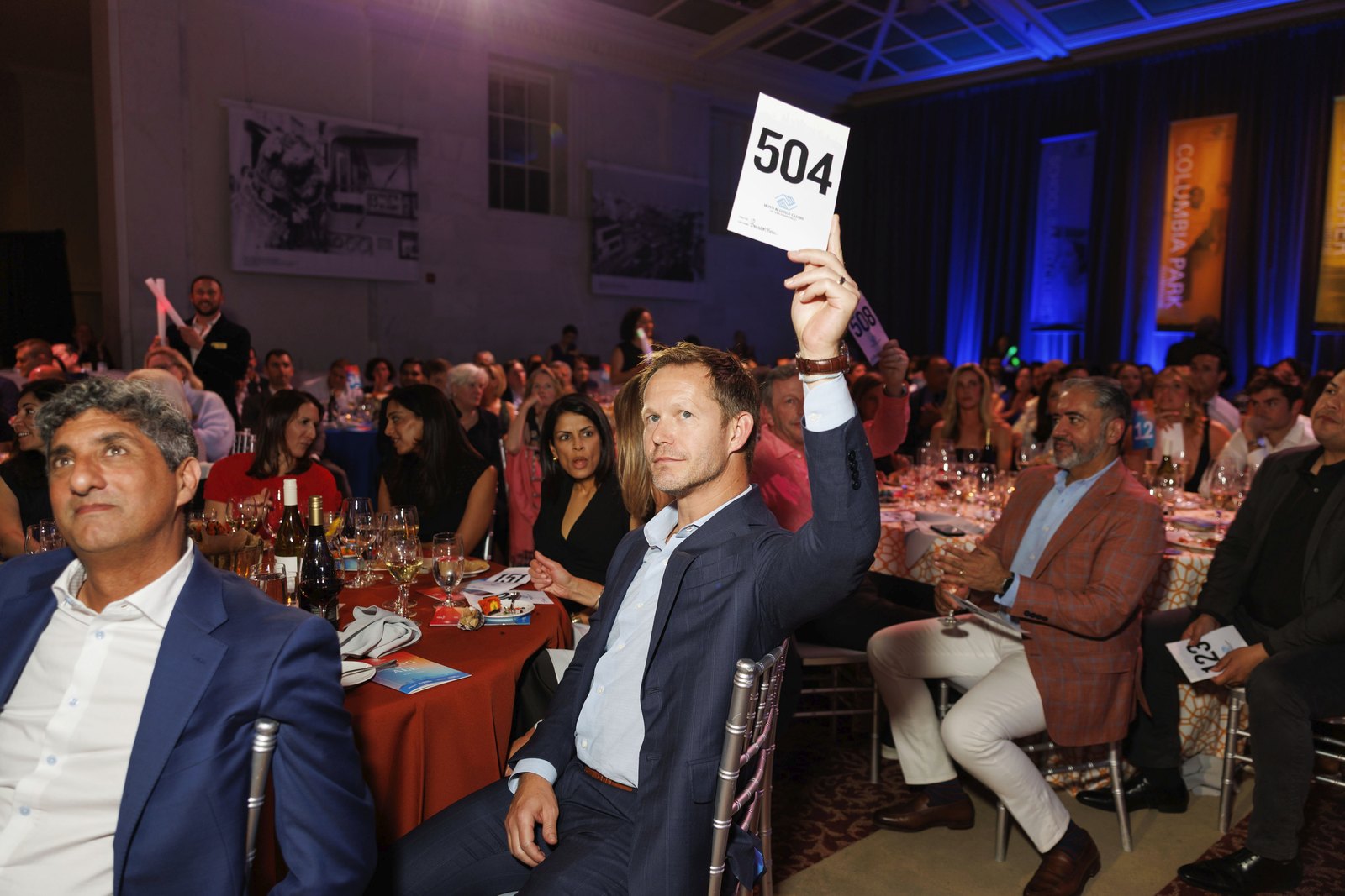 A gala guest raising auction paddle number 504 during a fundraising dinner