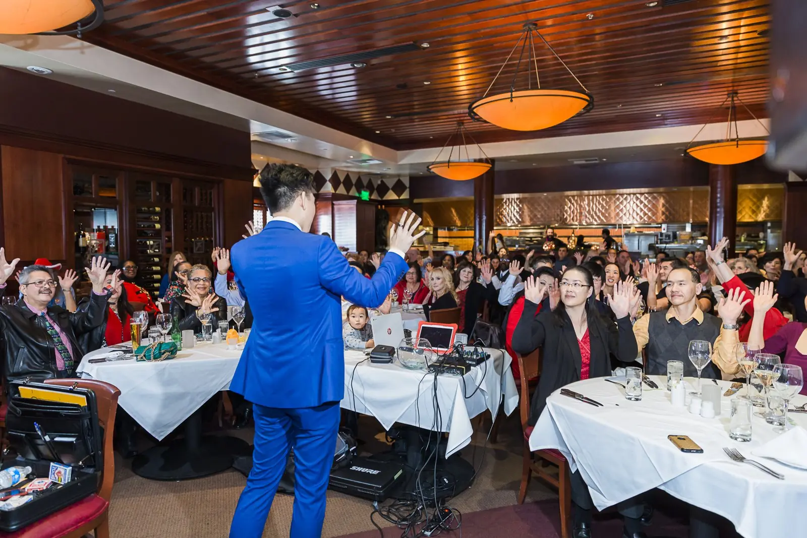 A corporate dinner audience raising their hands during Johnny Wu's show